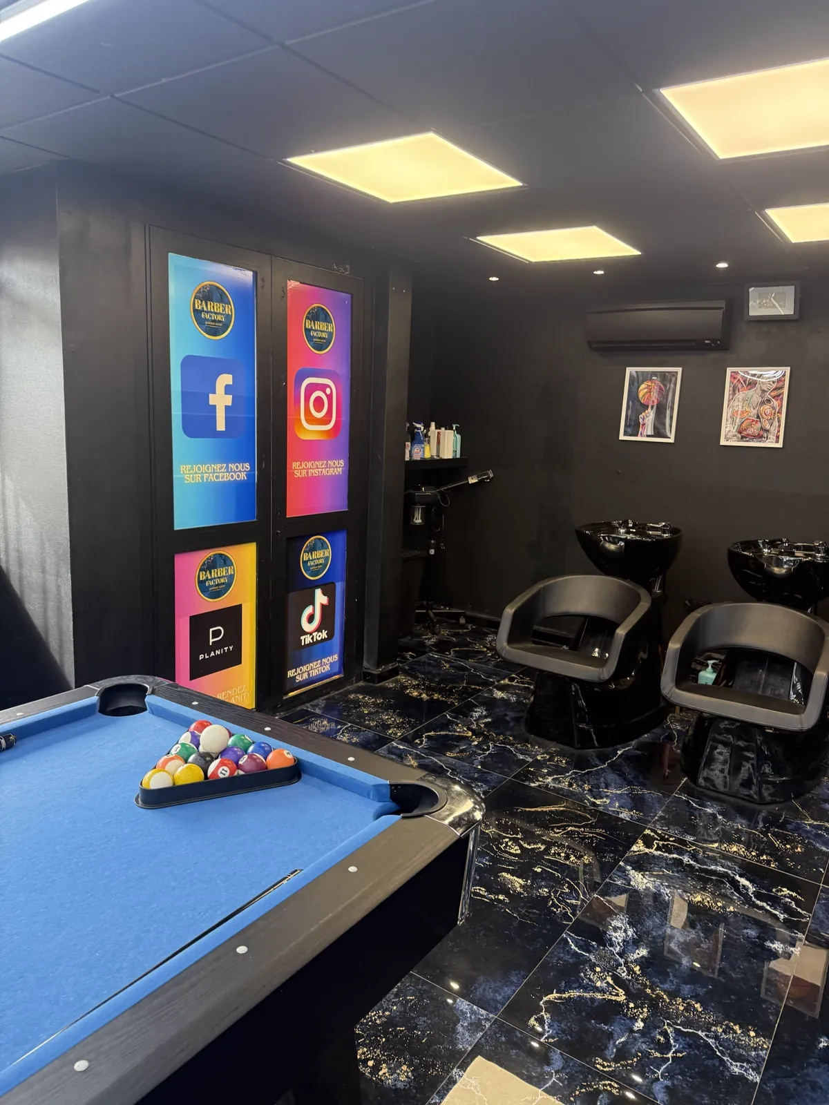 Billard, bacs à shampoing et panneaux réseaux sociaux du salon Barber Factory